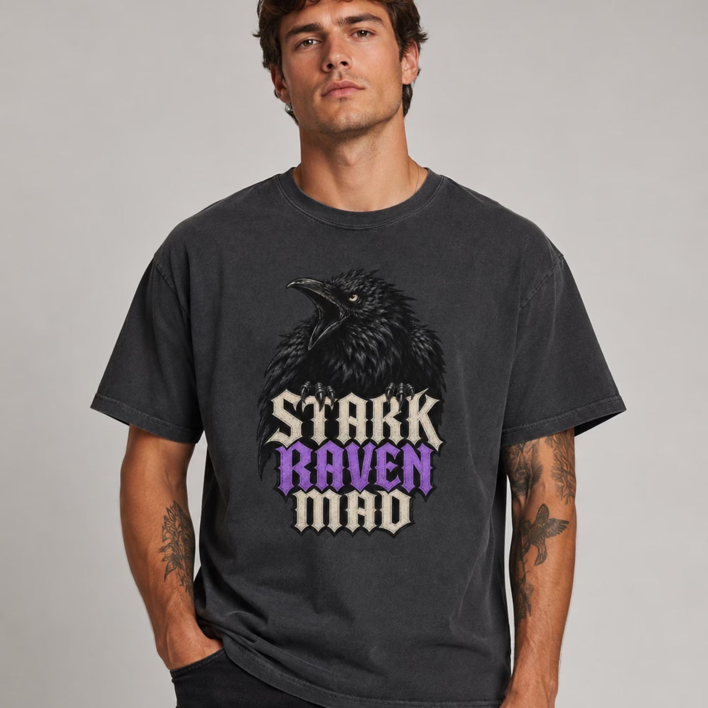 A man wearing a dark gray graphic t-shirt featuring a raven and the text 'STARK RAVEN MAD' in a stylized font, set against a plain light gray background.