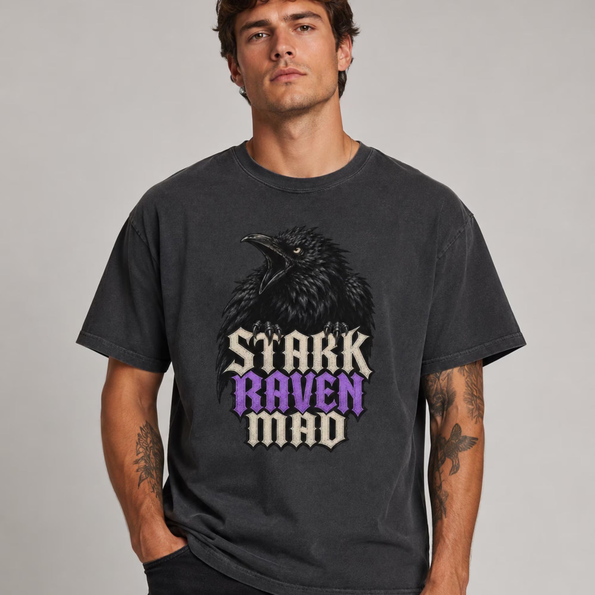 A man wearing a dark gray graphic t-shirt featuring a raven and the text 'STARK RAVEN MAD' in a stylized font, set against a plain light gray background.