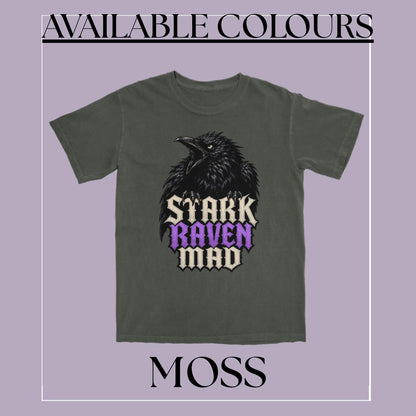 An olive green graphic t-shirt featuring a raven illustration and the text 'STARK RAVEN MAD' in black, beige, and purple. The image is framed with a light purple background, featuring the text 'AVAILABLE COLOURS' at the top and 'MOSS' at the bottom.