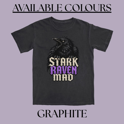 A dark gray t-shirt featuring a graphic of a raven with the text 'STARK RAVEN MAD' in cream and purple gothic lettering. The image is framed with the text 'AVAILABLE COLOURS' at the top and 'GRAPHHITE' at the bottom on a solid lavender background.