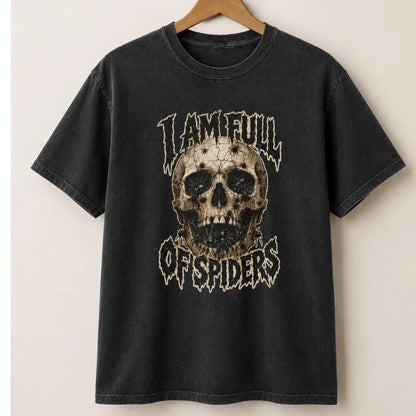 A black washed graphic t-shirt hanging on a wooden hanger against a light beige wall. The shirt features a distressed skull graphic in the center with the text 'I AM FULL OF SPIDERS' in a stylized white font.