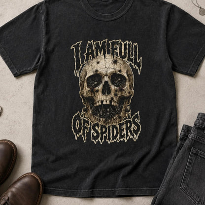 A black graphic t-shirt featuring a distressed skull design with the text 'I AM FULL OF SPIDERS' in a stylized font. The shirt is presented in a flat-lay arrangement alongside brown leather shoes, dark gray jeans, and rings on a textured concrete surface.