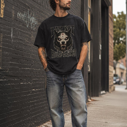 A man wearing a black graphic t-shirt with a wolf design and the words 'DOMINANT HOUSE TRAINED', paired with blue jeans, standing on a city sidewalk next to a dark brick wall.