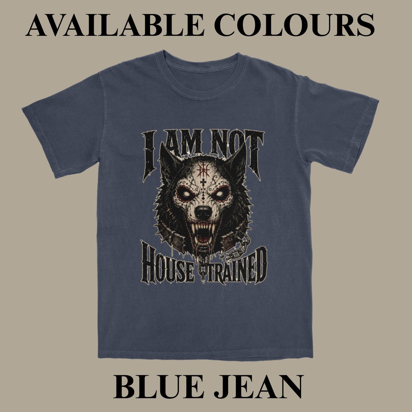 A blue-gray graphic t-shirt displayed against a solid taupe background with text overlays reading 'AVAILABLE COLOURS' at the top and 'BLUE JEAN' at the bottom. The t-shirt features a graphic of a snarling wolf with a cross on its forehead and the text 'I AM NOT HOUSE TRAINED'.