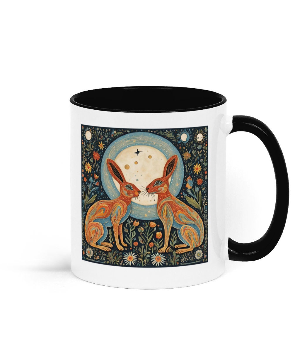 Witchy gifts, pagan gift. Moon goddess. A white 11 oz ceramic mug with a black interior and handle. It features a folk art design of two moon gazing hares facing each other under a full moon, adding a touch of whimsy and rustic charm to the mug.