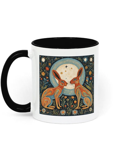 A white 11 oz ceramic mug with a black interior and handle. The mug showcases a folk art design of two moon gazing hares, sitting in reverence of the full moon&#39;s powerful glow, symbolizing the mystical connection between nature and lunar energy.