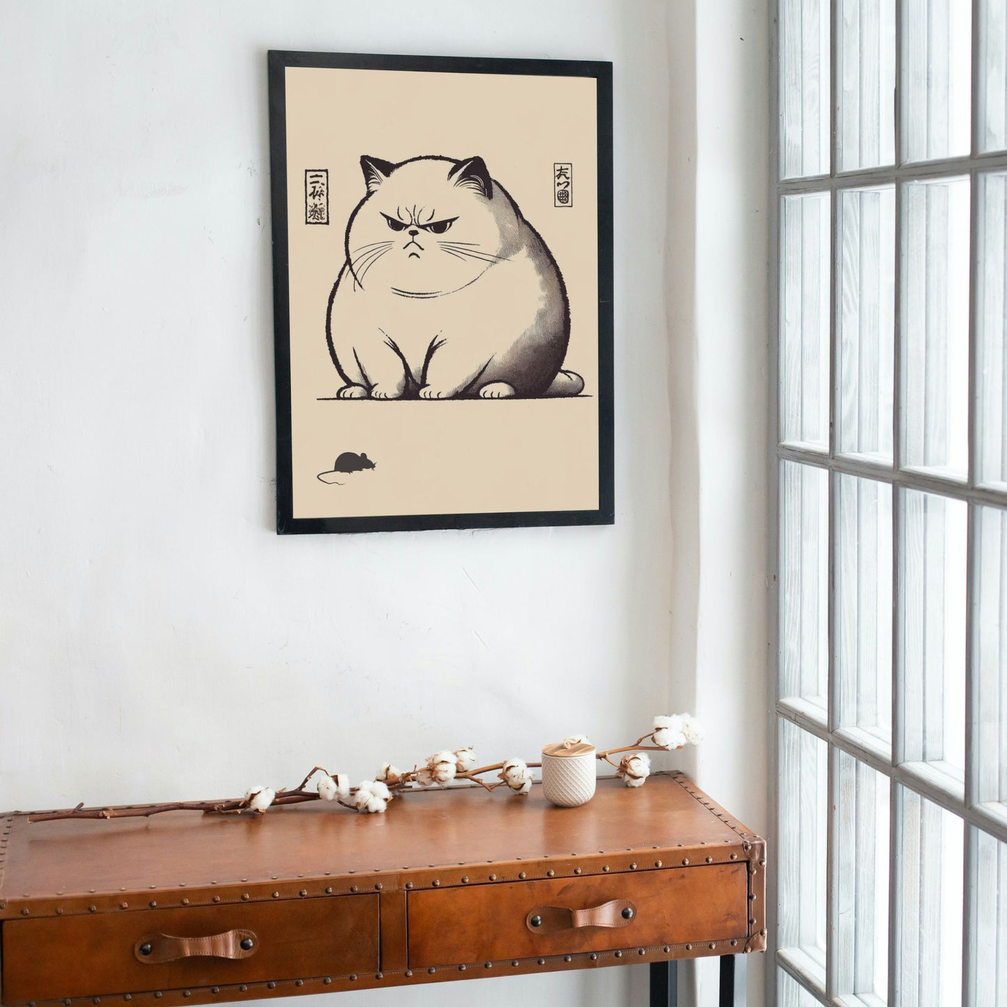 Modern interior scene with unimpressed cat art print hanging above a wooden sideboard with plants.