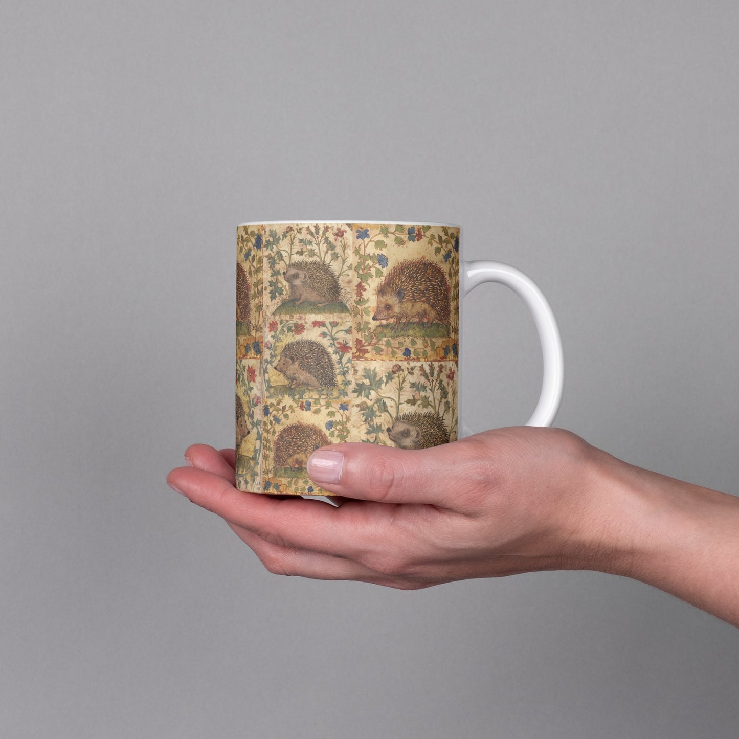 A white ceramic mug with a wraparound hedgehog and floral design inspired by medieval manuscripts