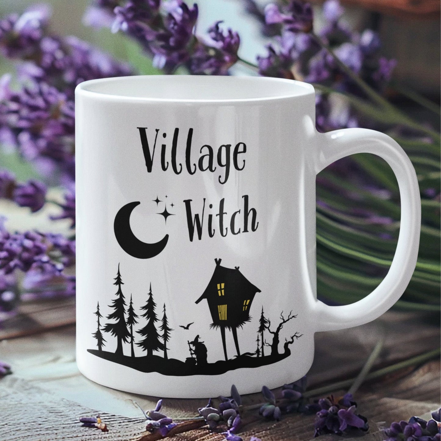 11oz white mug with a black silhouette design of a witch outside with a cauldron and trees. There is a rickety house on stilts with light coming through the windows with a moon and stars in the sky. The text says Village Witch.