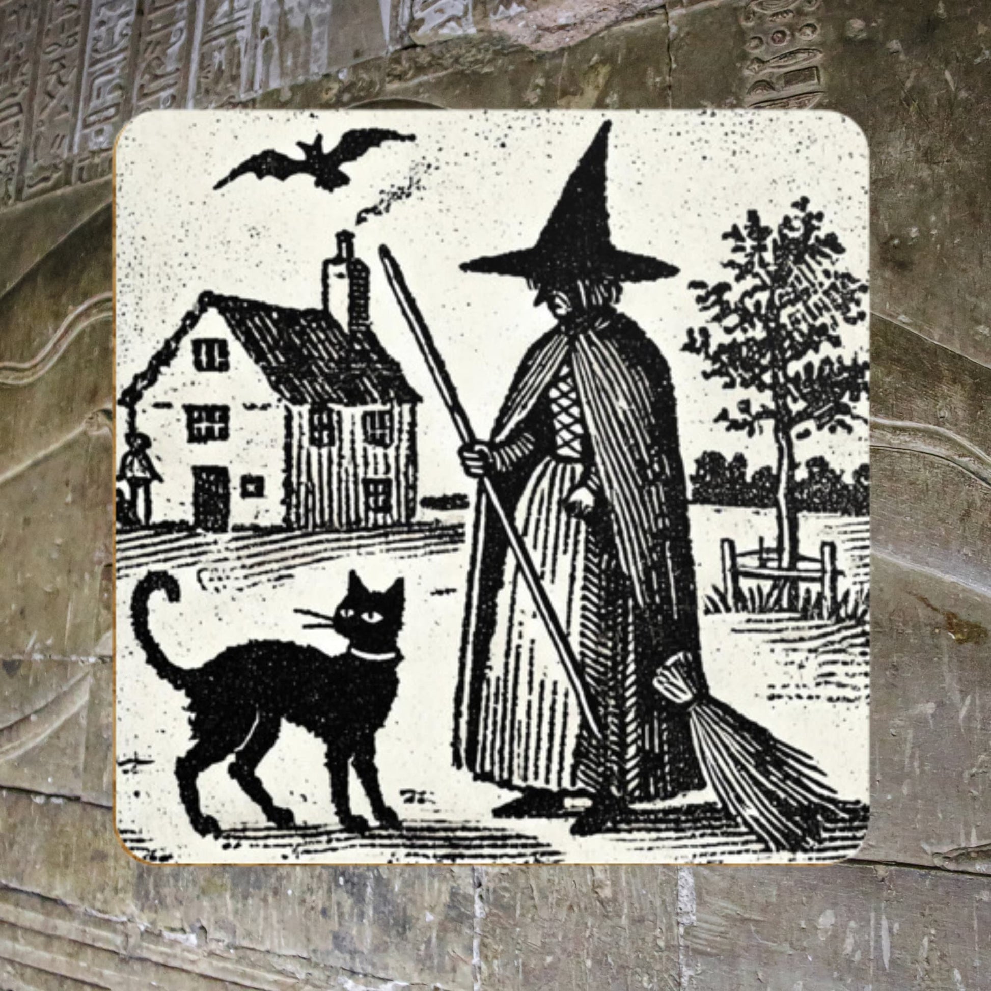 Dark academia, witchy gifts: woodcut of a witch with her familiar, a black cat printed on a cork backed, hardwood coaster. Witches house, home in the background with black cat wearing a collar. Set of four.
