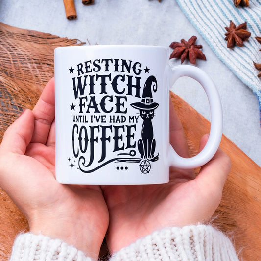 white 11oz ceramic mug with different sized fonts - &#39;resting witch face until I&#39;ve had my coffee&#39;. There is a design of a black cat wearing a witches hat to one side and star embellishments and a pentacle. A great witchy gift.