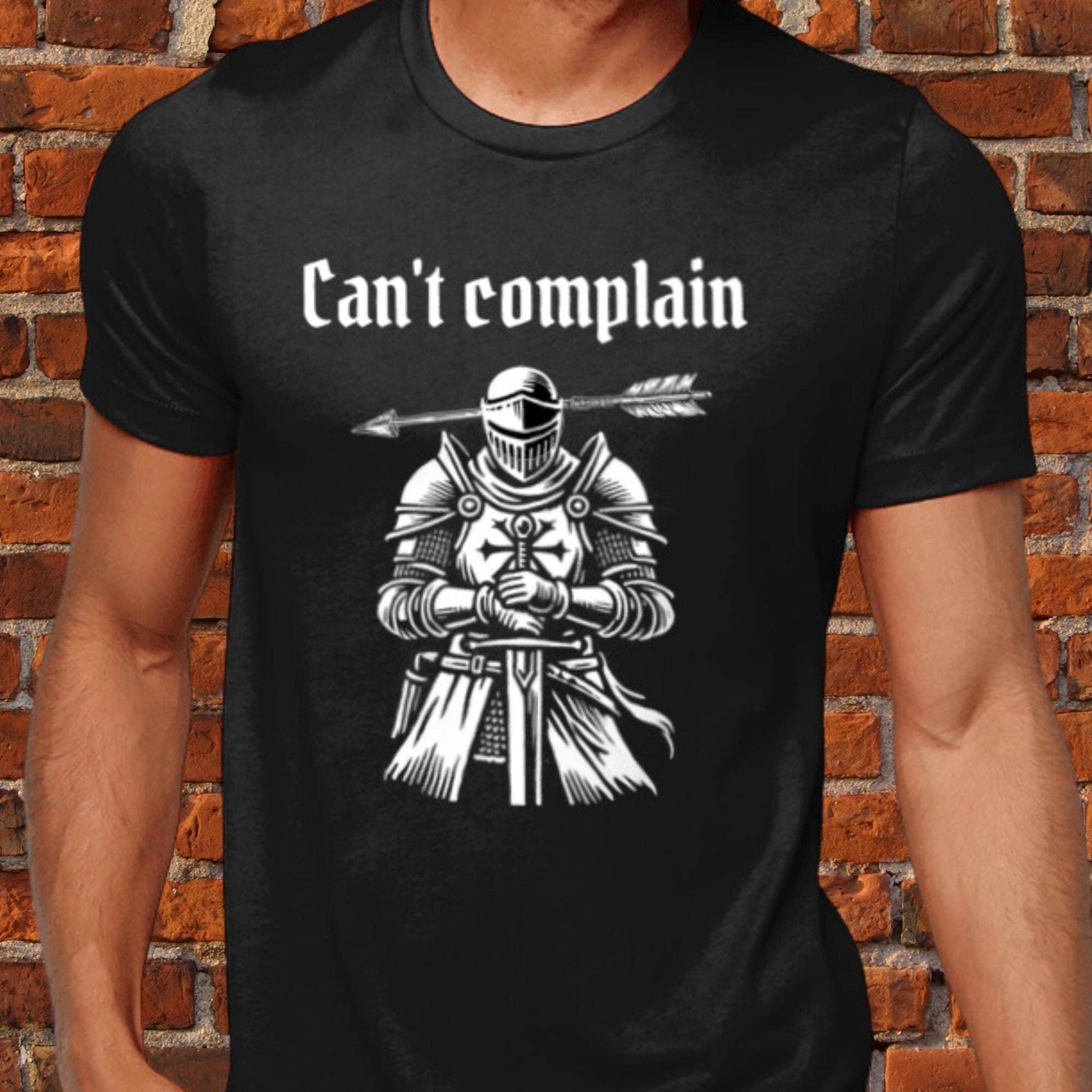 Unisex dark humour t-shirt featuring a sarcastic medieval woodcut of a knight with an arrow through his head and the phrase &quot;Can&#39;t Complain.&quot; 100% cotton, offering luxurious softness and a modern fit. Perfect for fans of quirky, gothic humour.
