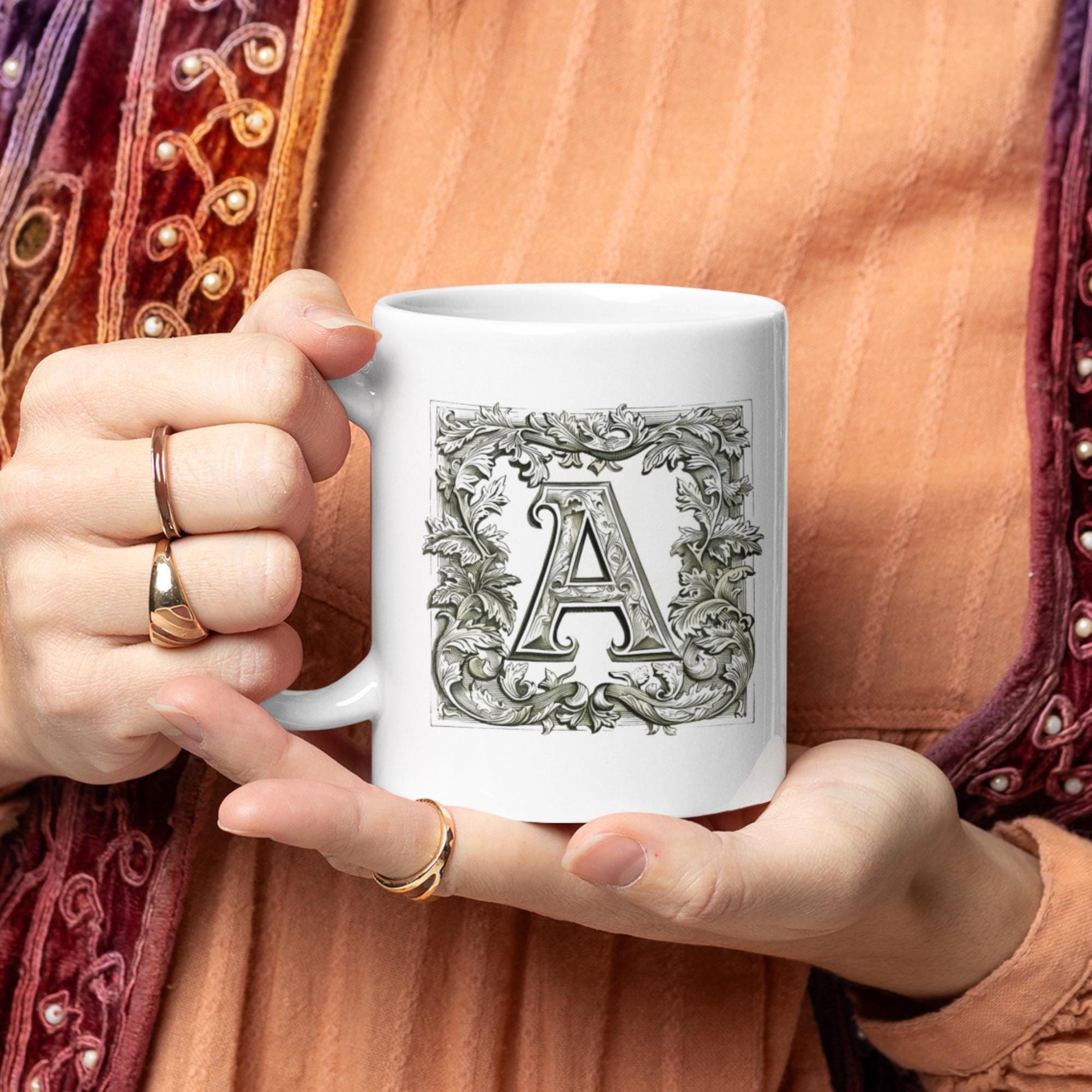 Charming mug adorned with a monogram letter styled in calligraphy, framed by an ornate, manuscript-like floral border