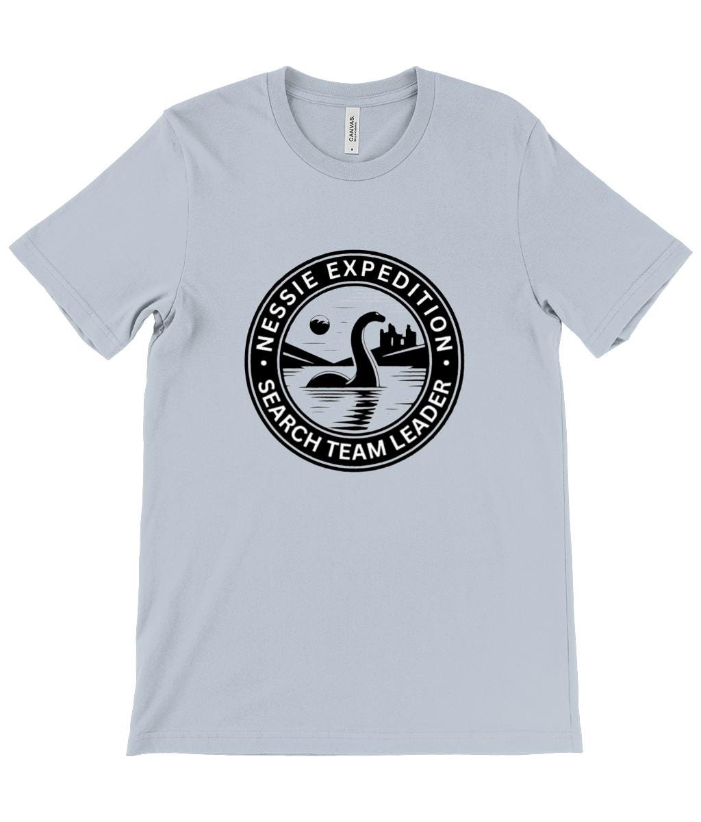 Loch Ness Monster Emblem T-Shirt - A bold design showcasing the legendary Nessie emerging from the lake, with a mysterious castle silhouette and night time scene.