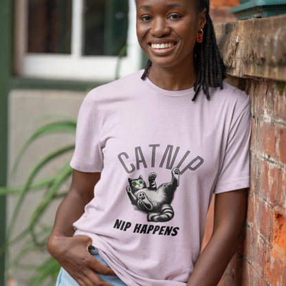 Graphic t-shirt showing a cute illustration of a cat with green eyes, looking surprised while lying on its back. The words CATNIP and NIP HAPPENS are prominently displayed, creating a fun and witty design.