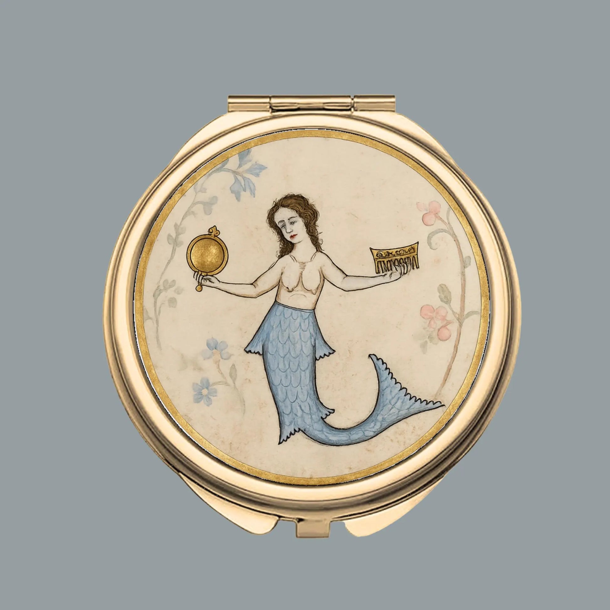 A round gold-toned compact mirror featuring a vintage-style illustration of a mermaid with a blue tail holding a gold mirror and a book, set against a light gray background.